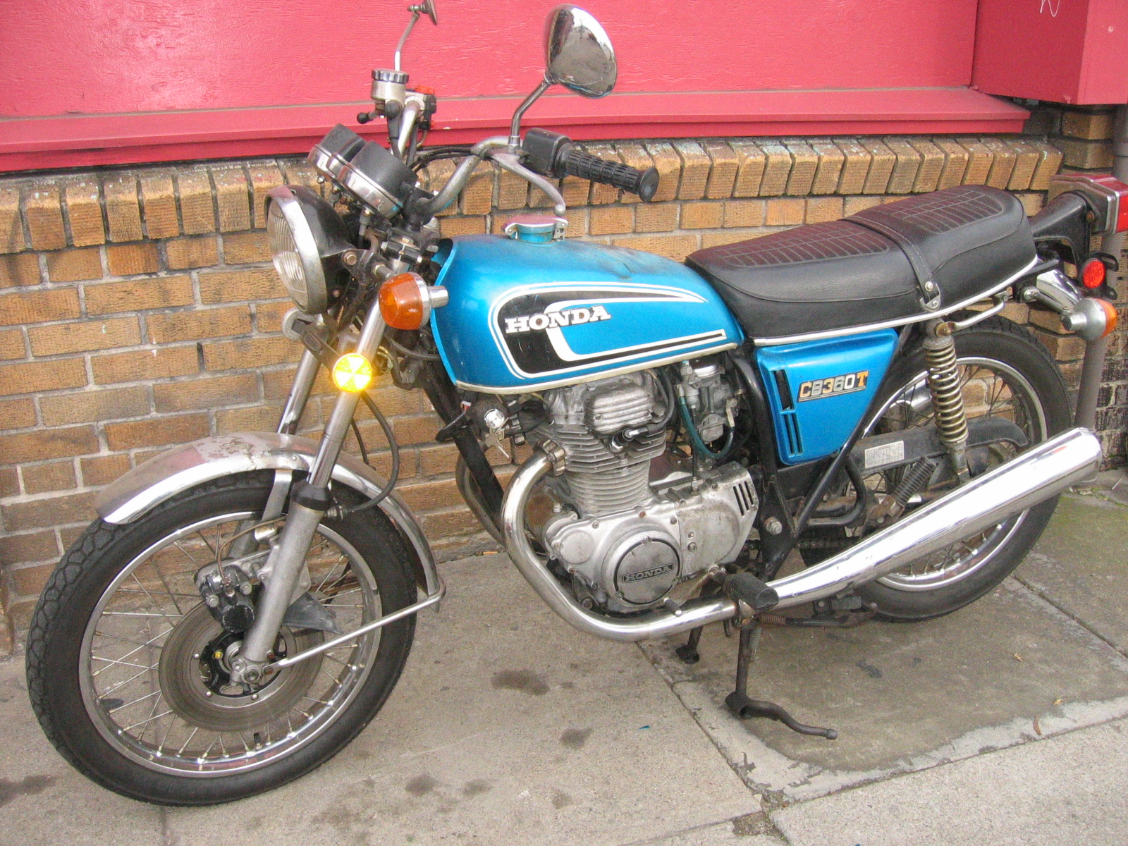 Blue Honda CB360T parked in front of a brick wall