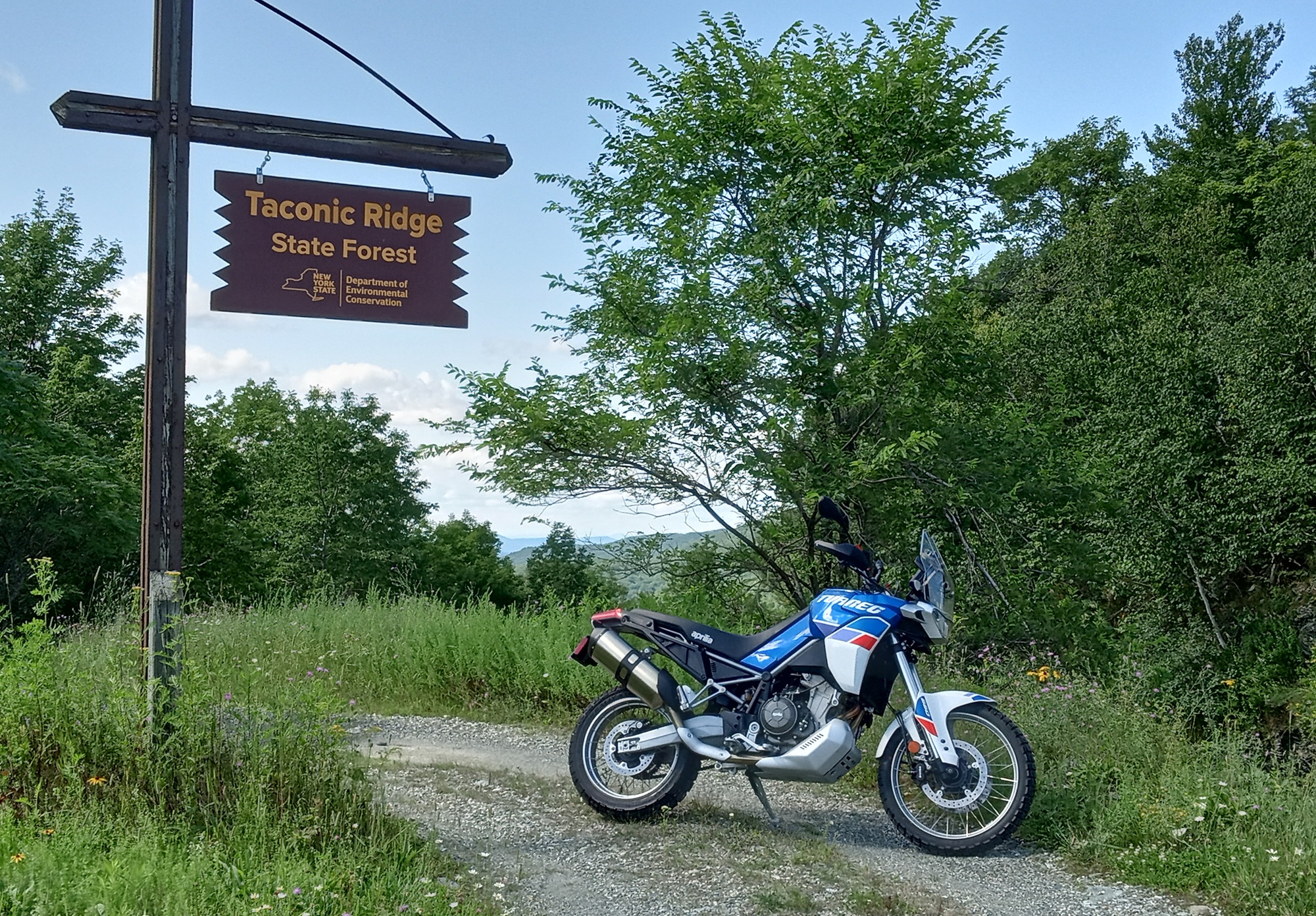 white, red, and blue Aprilia Tuareg 660 parked on an overlook along a curving mountain road
