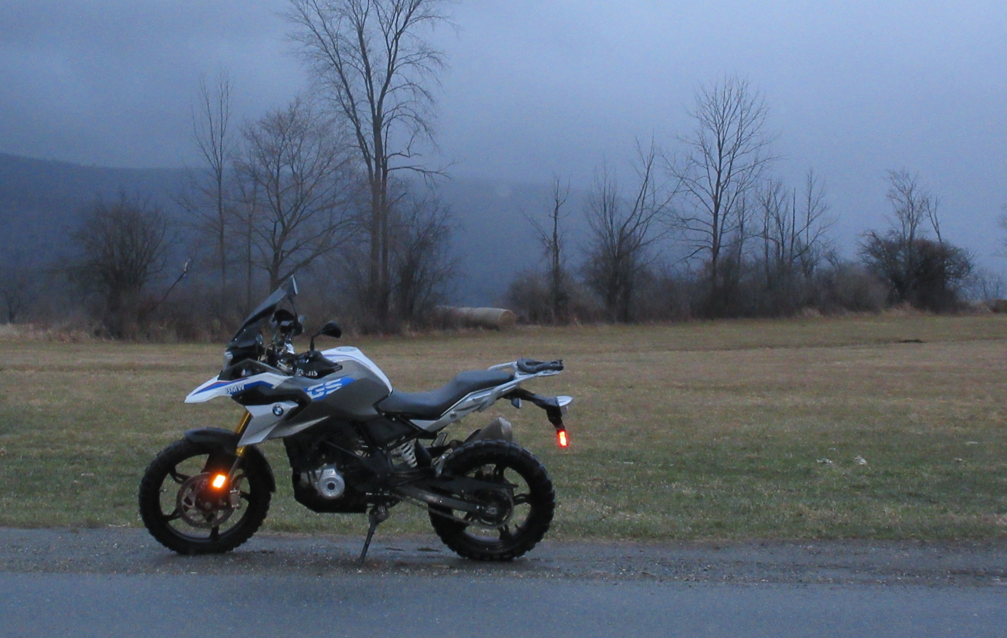 BMW G 310 GS alongside a country road on a dreary day with fog shrouding the brown and gray mountains in the distance