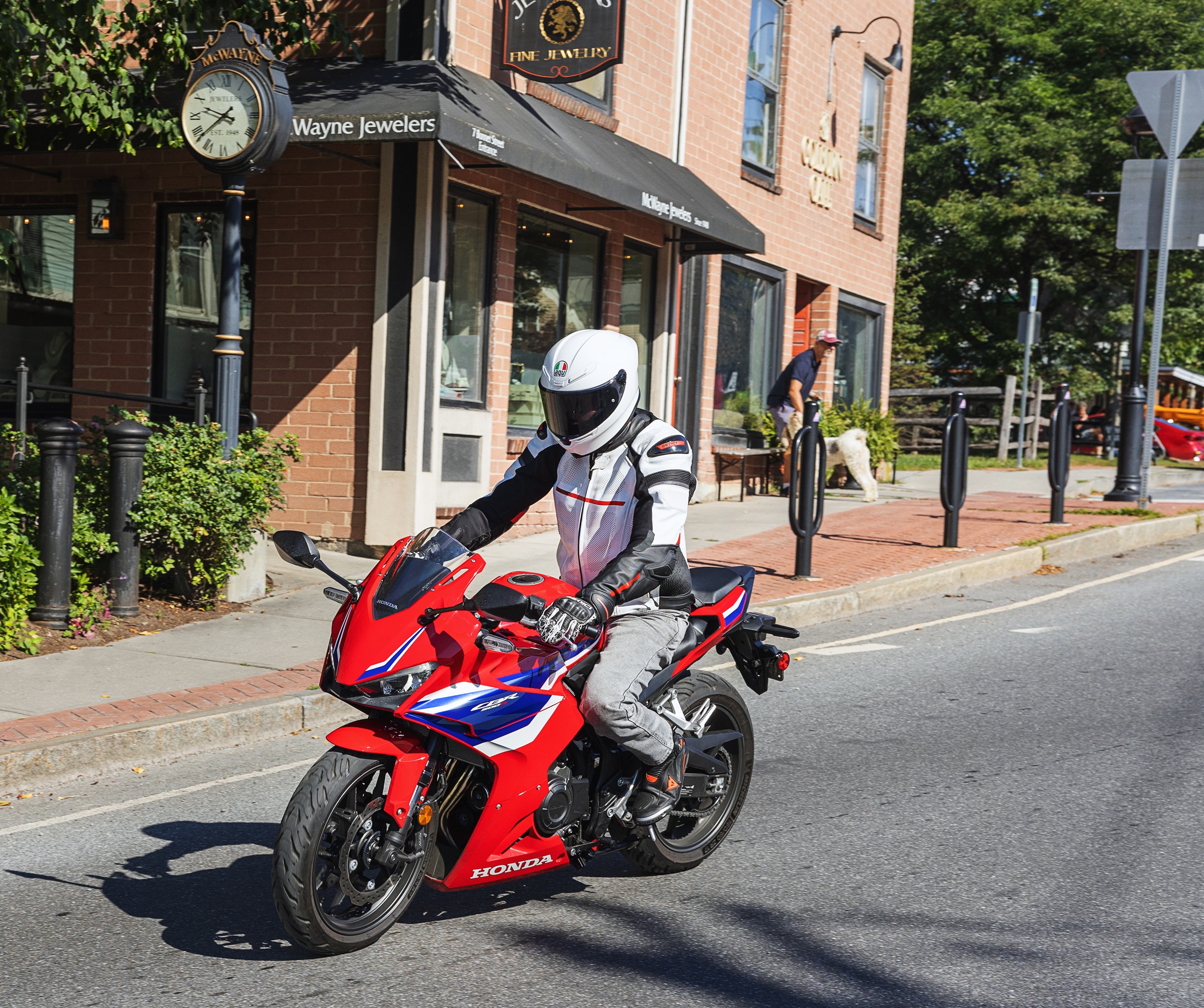 riding the red Honda CBR500R past a jewelry store storefront in town