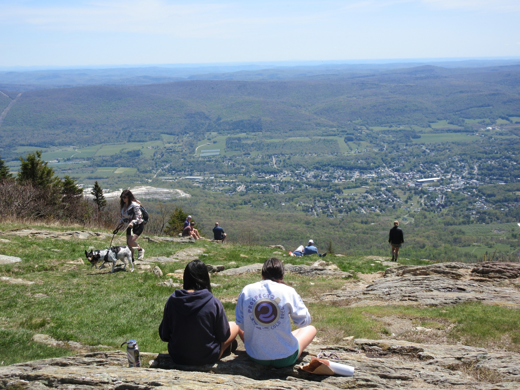 people sit on the grass at the top of Mount Greylock and admire the view to the east of mountains filing off into the distance