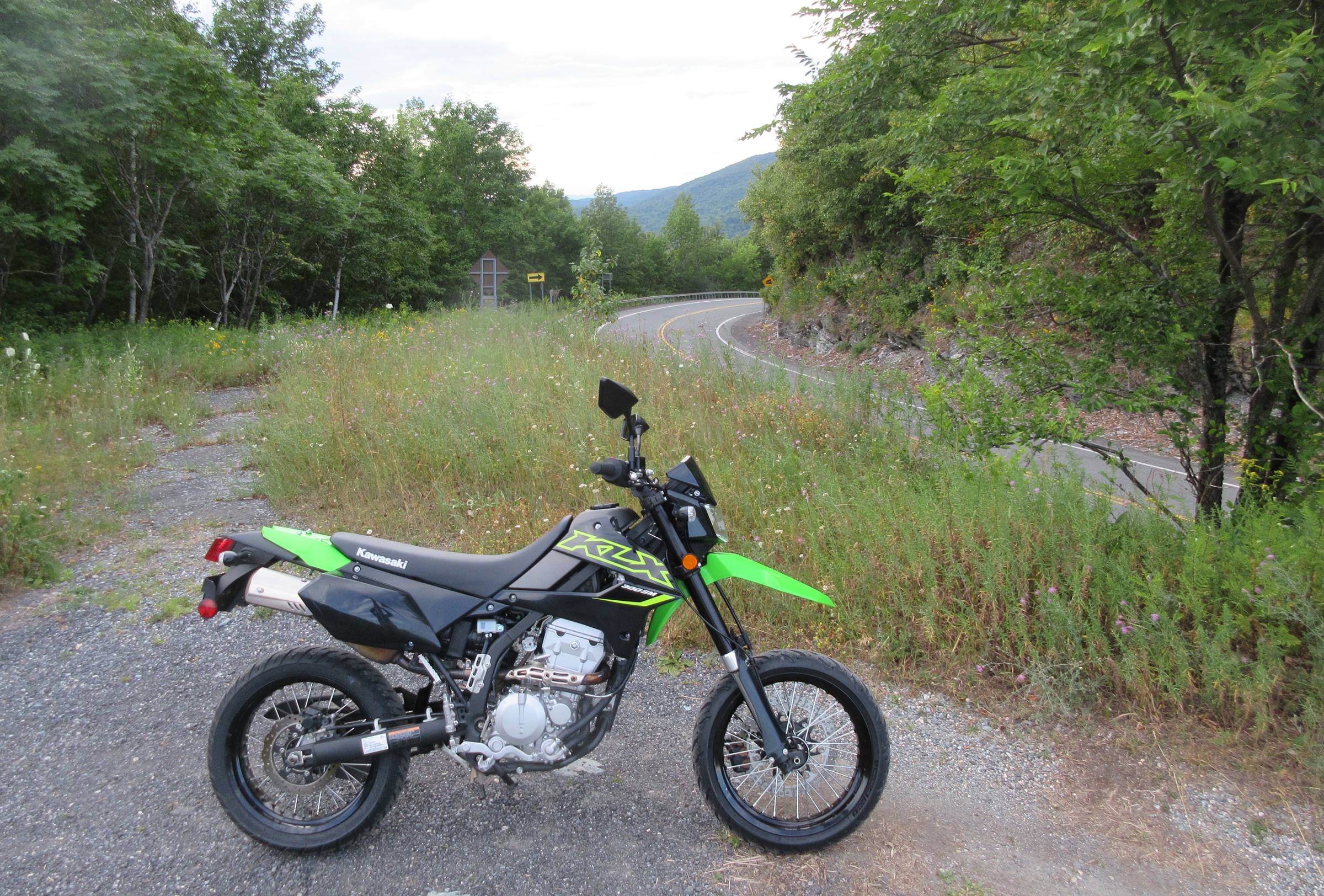green and black KLX300sM parked on an overlook along a curving mountain road