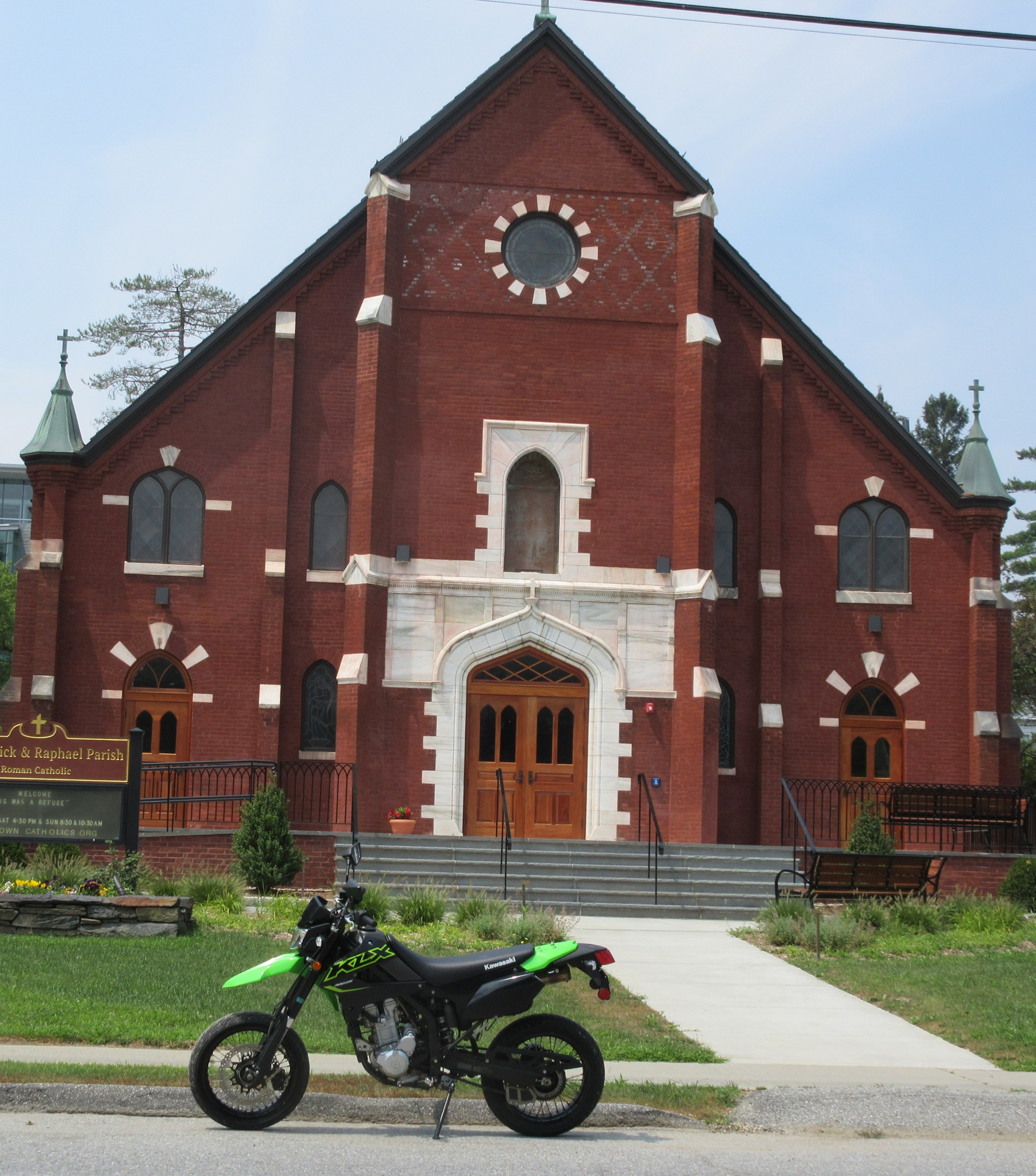 green and black supermoto KLX300SM in front of a small-town brick church
