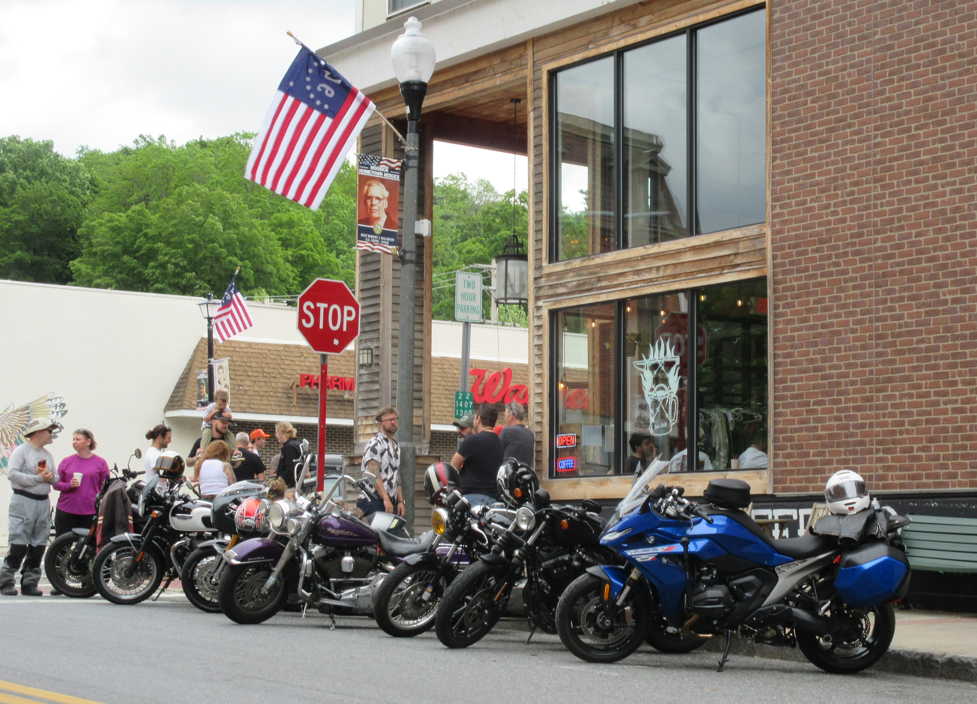 group of people drinking coffee and talking beside a row of motorcycles on a small-town street