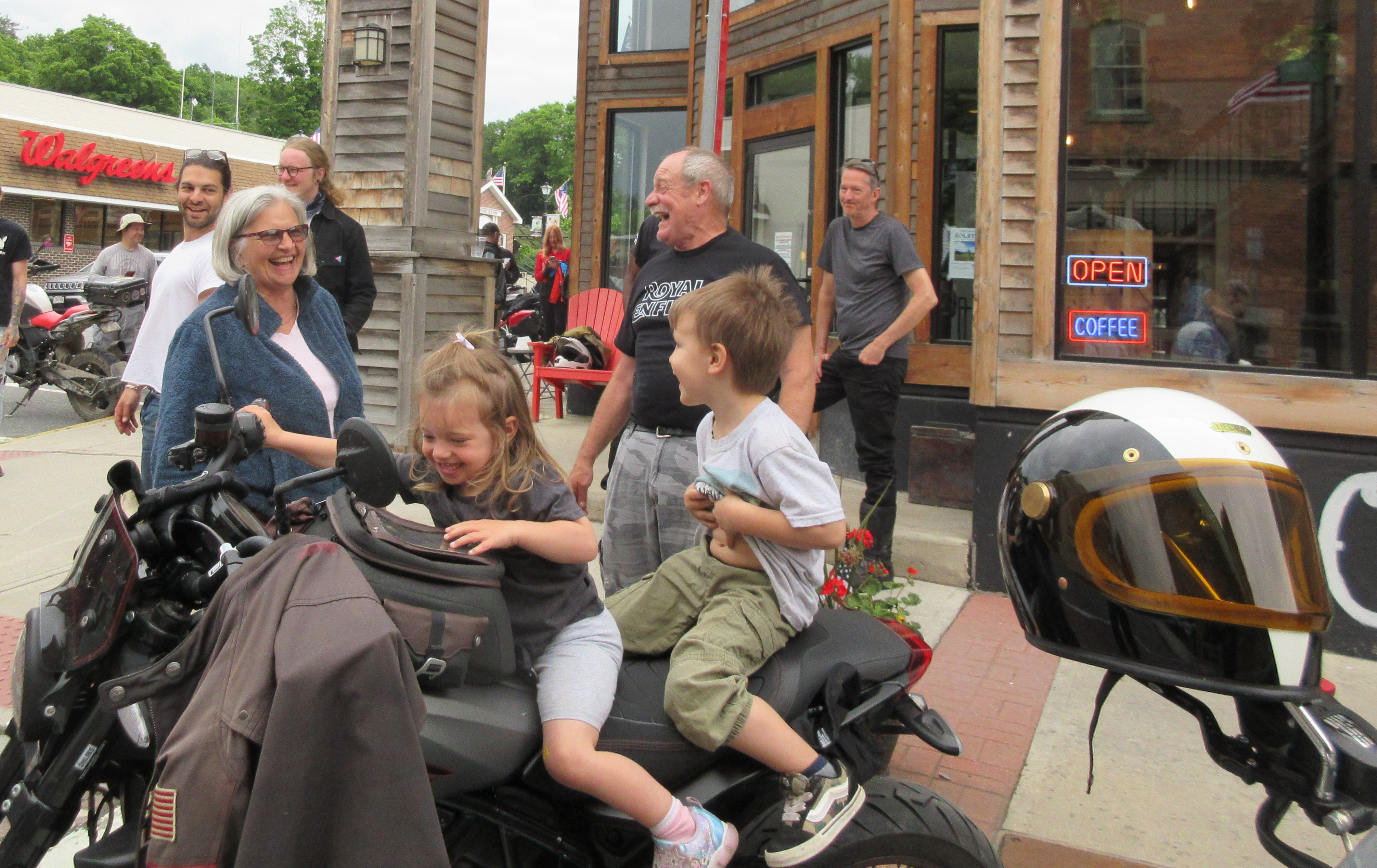 onlookers smile and laugh as two small children test-sit a motorcycle at The Moto Social event