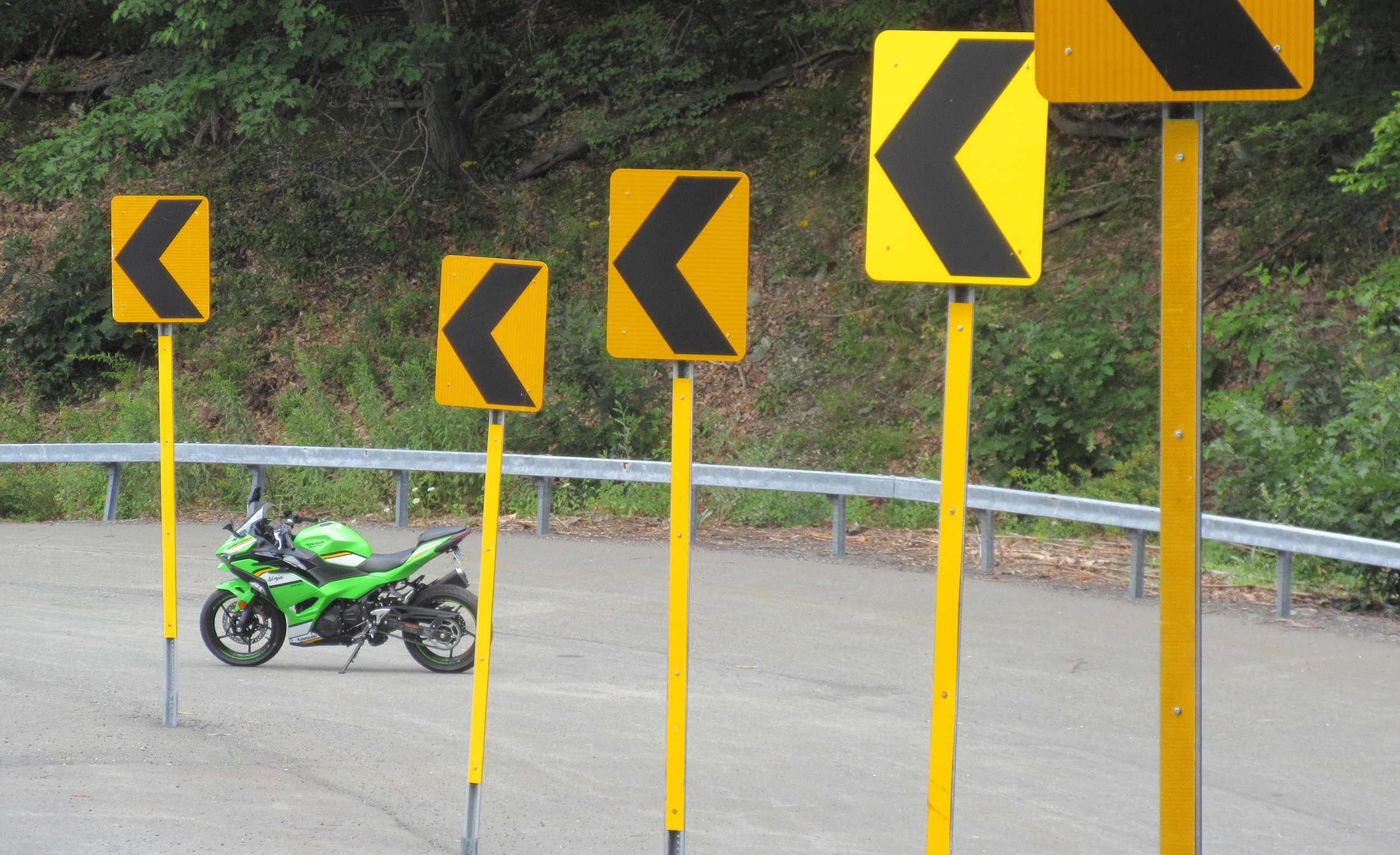 Green Ninja 500 parked on a curve with a row of curve warning signs