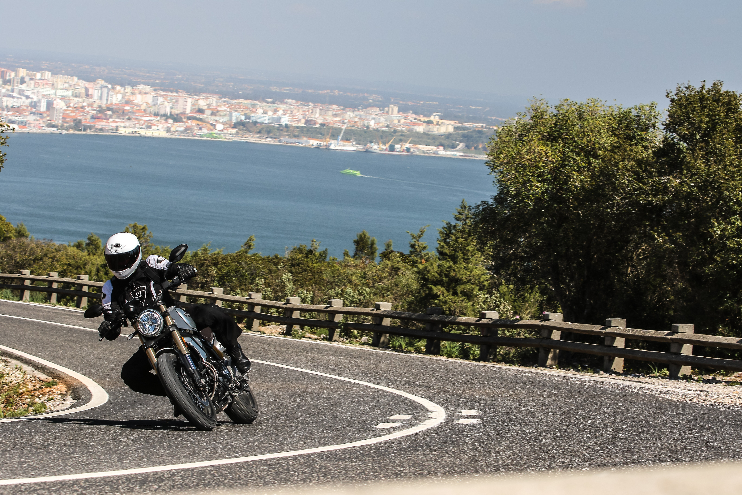 riding a Ducati Scrambler 1100 on a curve on a mountain road with Lisbon, Portugal, in the background