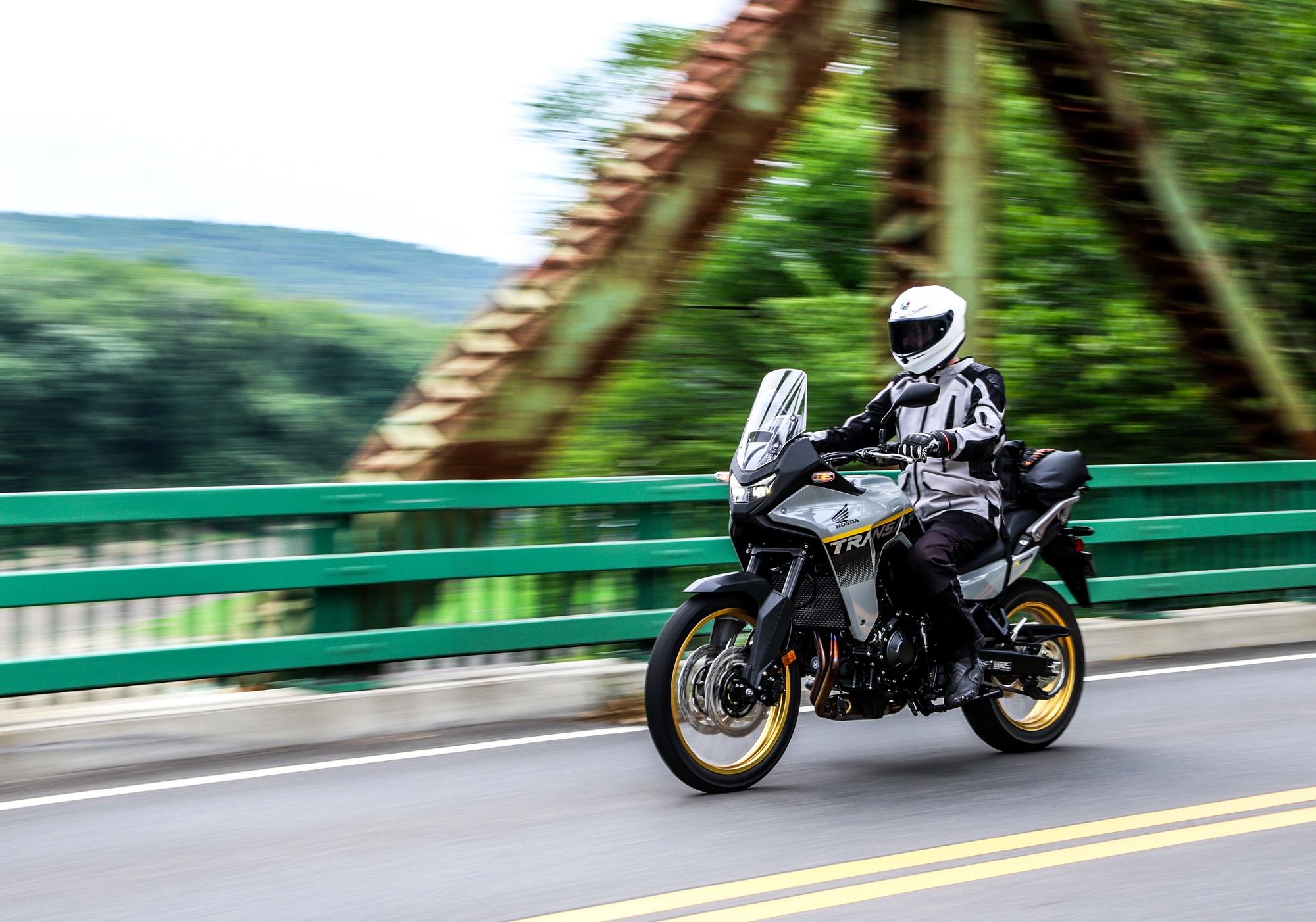riding a gray Honda Transalp across an old bridge, loaded up with luggage on the bike