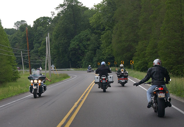 several riders on the road, waving to a passing rider